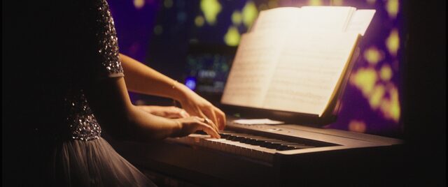 Hände einer Pianistin auf den Tasten, daneben beleuchtete Noten