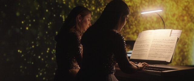 Zwei Pianistinnen im Profil an einem Flügel, davor beleuchtete Noten